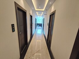 Un pasillo moderno de hotel con piso de mármol, puertas oscuras e iluminación empotrada en el techo.