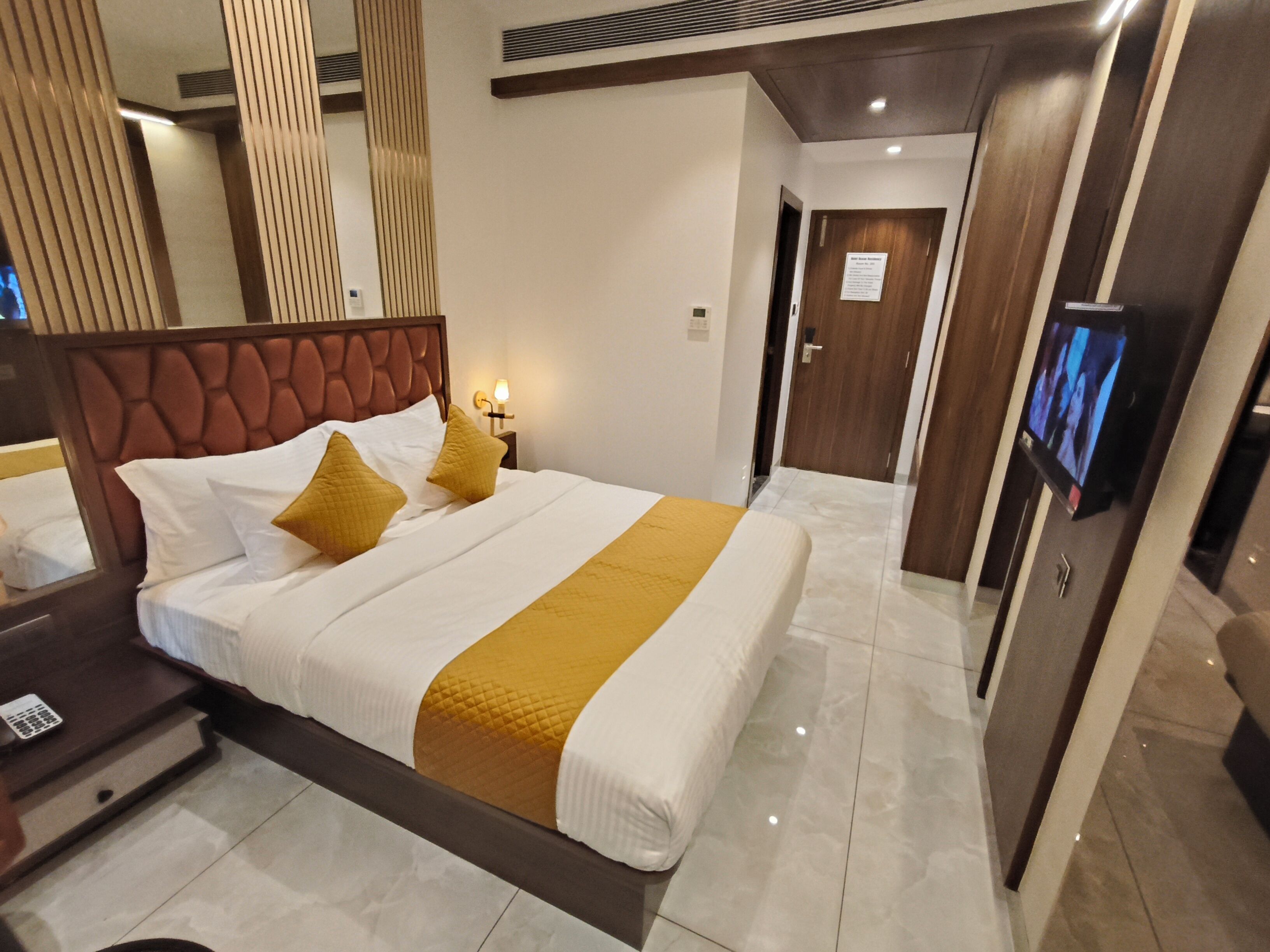 A hotel room with a large bed, a nightstand, a television, and a door leading to another room.