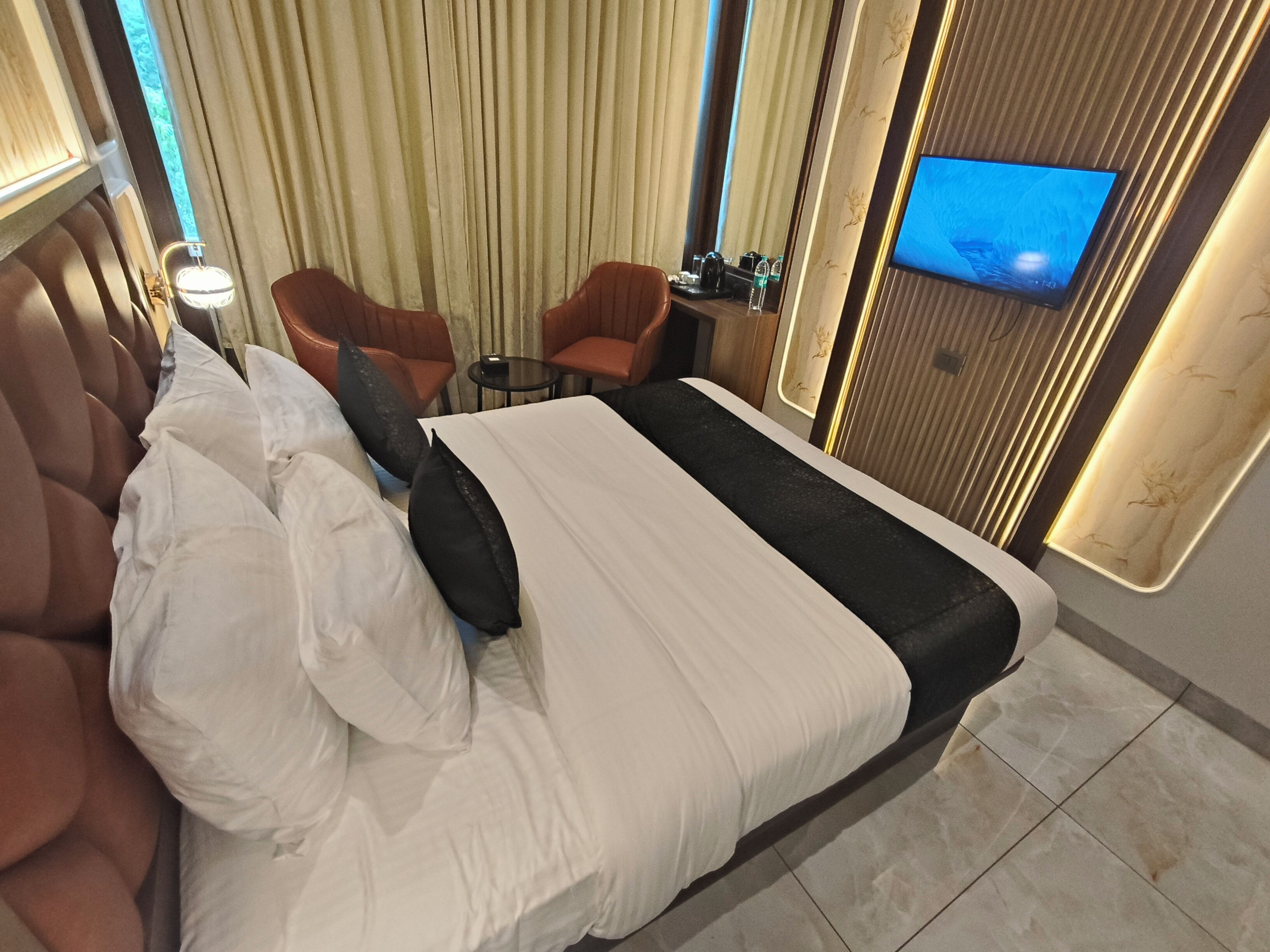 A hotel room with a large bed, a TV on the wall, a small table, and two chairs.