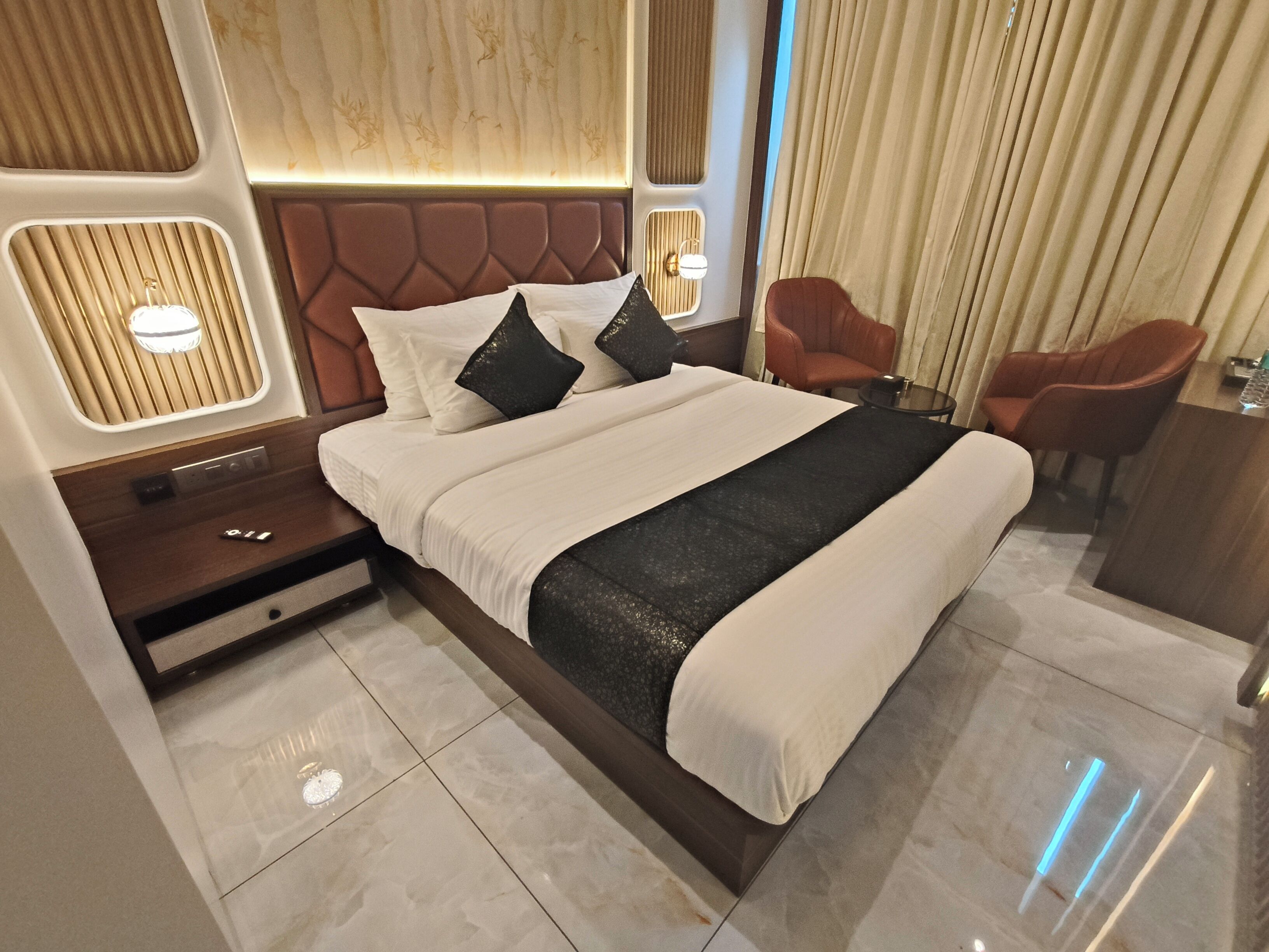 A modern hotel room with a large bed, a nightstand, a desk, and two chairs.