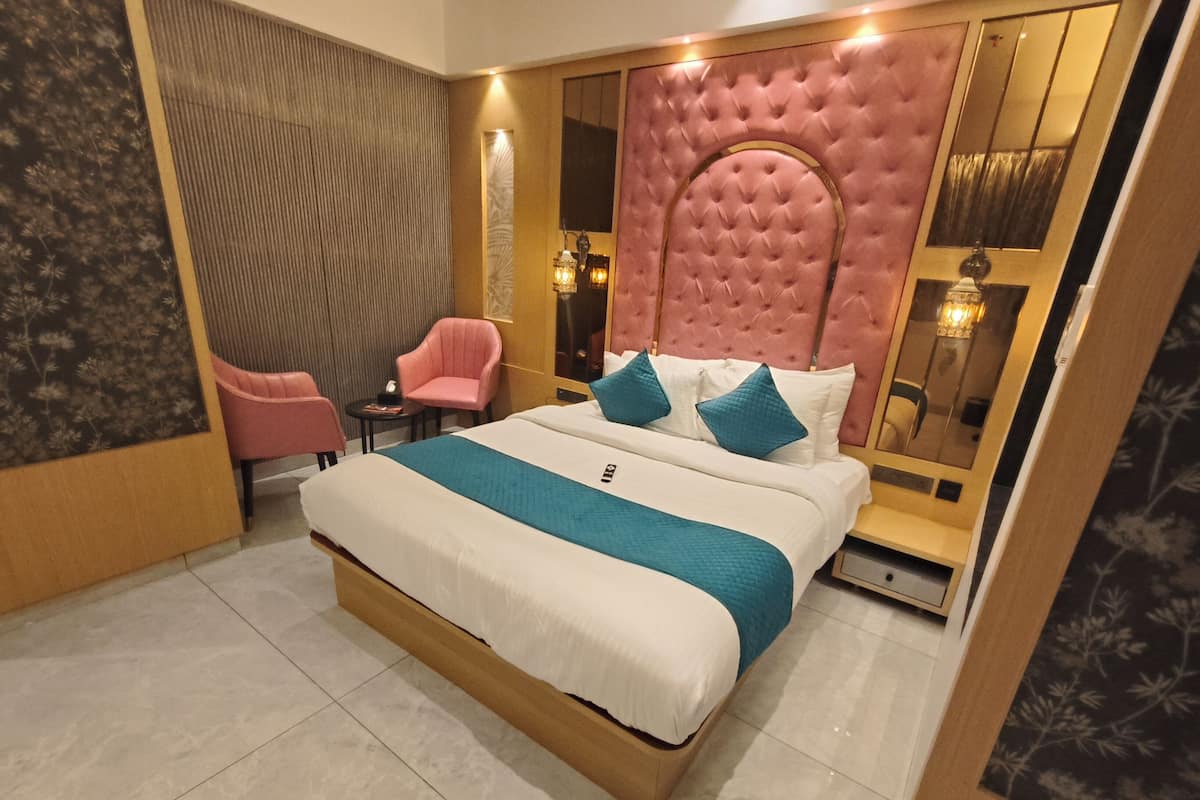 Ein modernes Hotelzimmer mit einem großen Bett, einem rosa Sessel, einem kleinen Tisch und einem Spiegel.