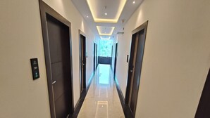 A modern hotel corridor with a marble floor, dark doors, and recessed lighting.
