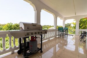 A covered patio with a barbecue grill, a gas cylinder, and outdoor seating.