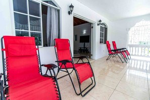 Un espace extérieur abrité, aménagé avec des chaises rouges et un sol carrelé.