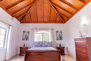 Une chambre à coucher avec un plafond en bois, un lit, deux tables de chevet, une commode et deux tableaux accrochés au mur.