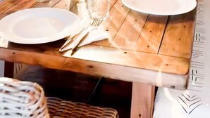 Un comedor con una mesa de madera dispuesta para una comida, rodeado de sillas de mimbre y una lámpara colgante.