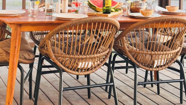 Una terraza de madera con sillas de mimbre, una mesa lista para comer y luces colgantes.