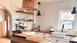 Una cocina con una mesa de madera rústica, armarios blancos y una lámpara colgante de mimbre.