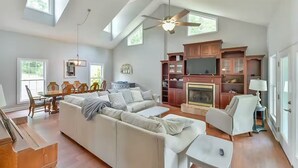 A spacious living room with a high ceiling, a fireplace, and a dining area with wooden furniture.