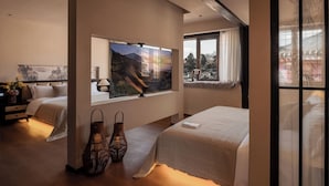 Habitación de hotel con un televisor grande, dos camas, un ventanal con vistas y jarrones decorativos.