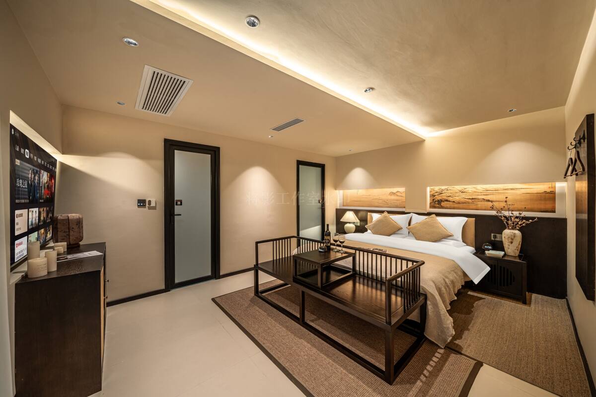Ein modernes Hotelzimmer mit Bett, Nachttisch, Lampe und einem kleinen Schreibtisch mit Stuhl.
