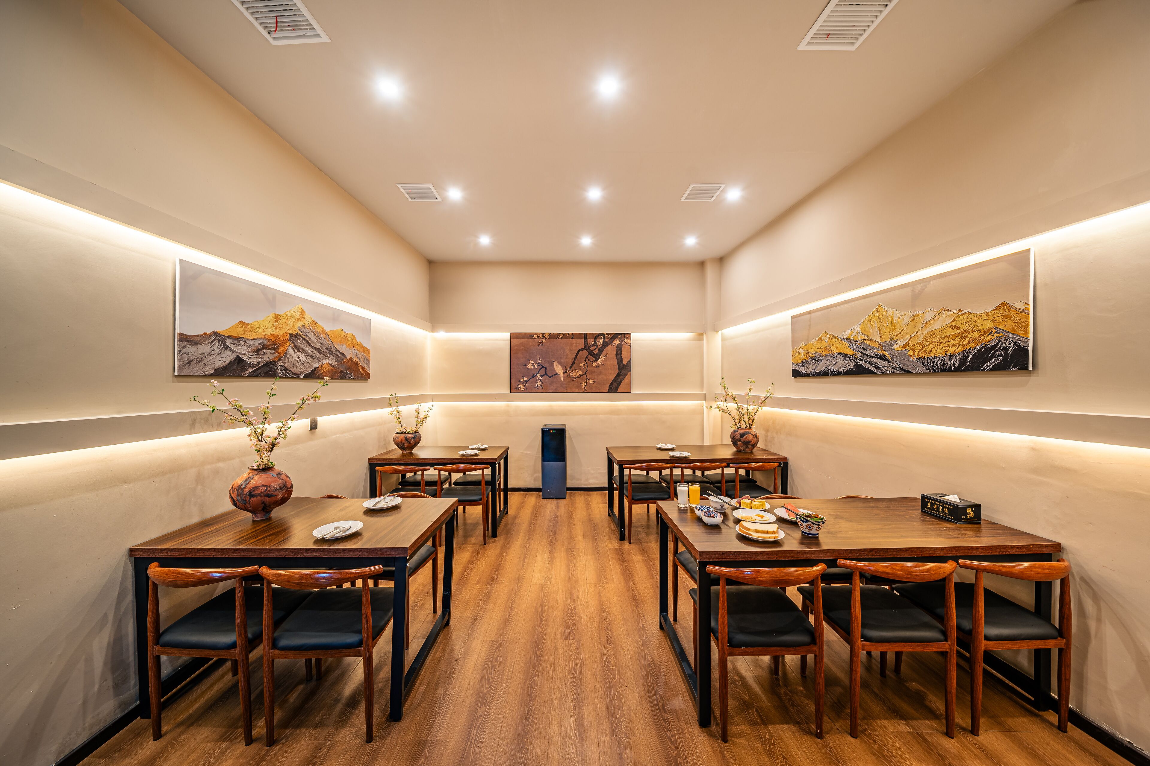 A dining area with wooden tables and chairs, a central pillar, and artwork on the walls.