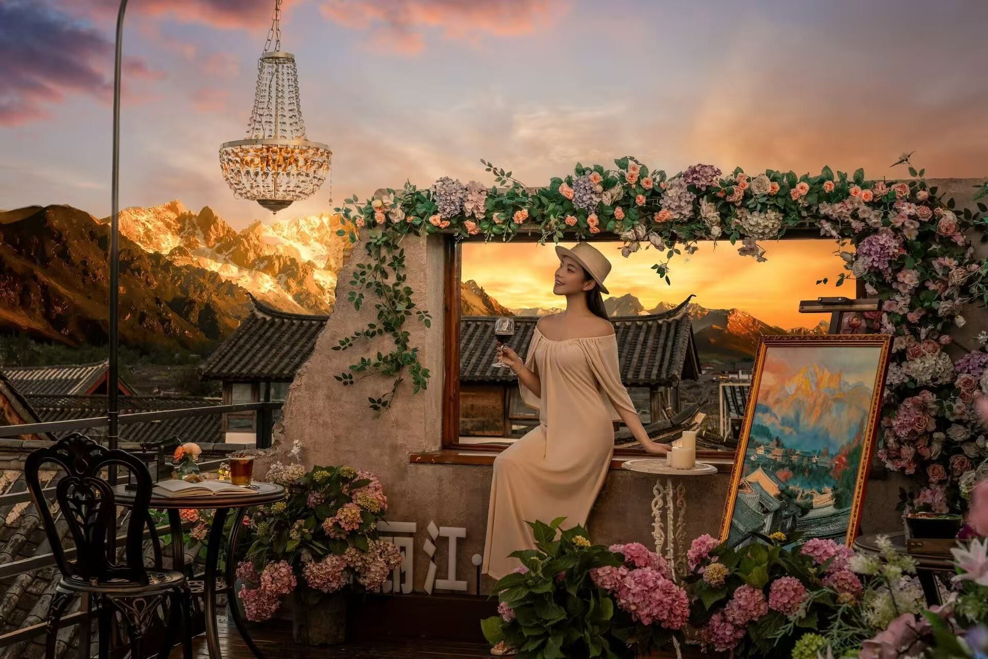 En kvinde i kjole står ved et bord med et drikkebreve, omgivet af blomster og et maleri, med traditionel arkitektur og bjerge i baggrunden.
