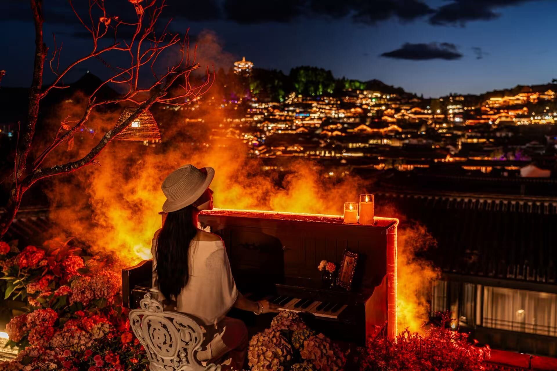 A piano with a candle and flowers, overlooking a cityscape at night.