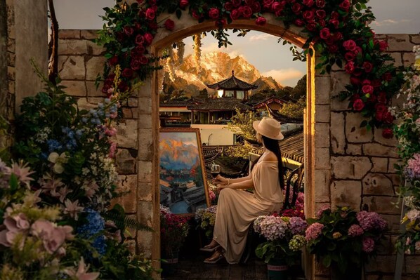 Una donna seduta sotto un arco di pietra con un dipinto, circondata da fiori.