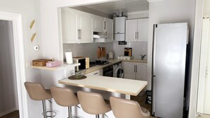 A compact kitchen with a central island, bar stools, a washing machine, and a refrigerator.