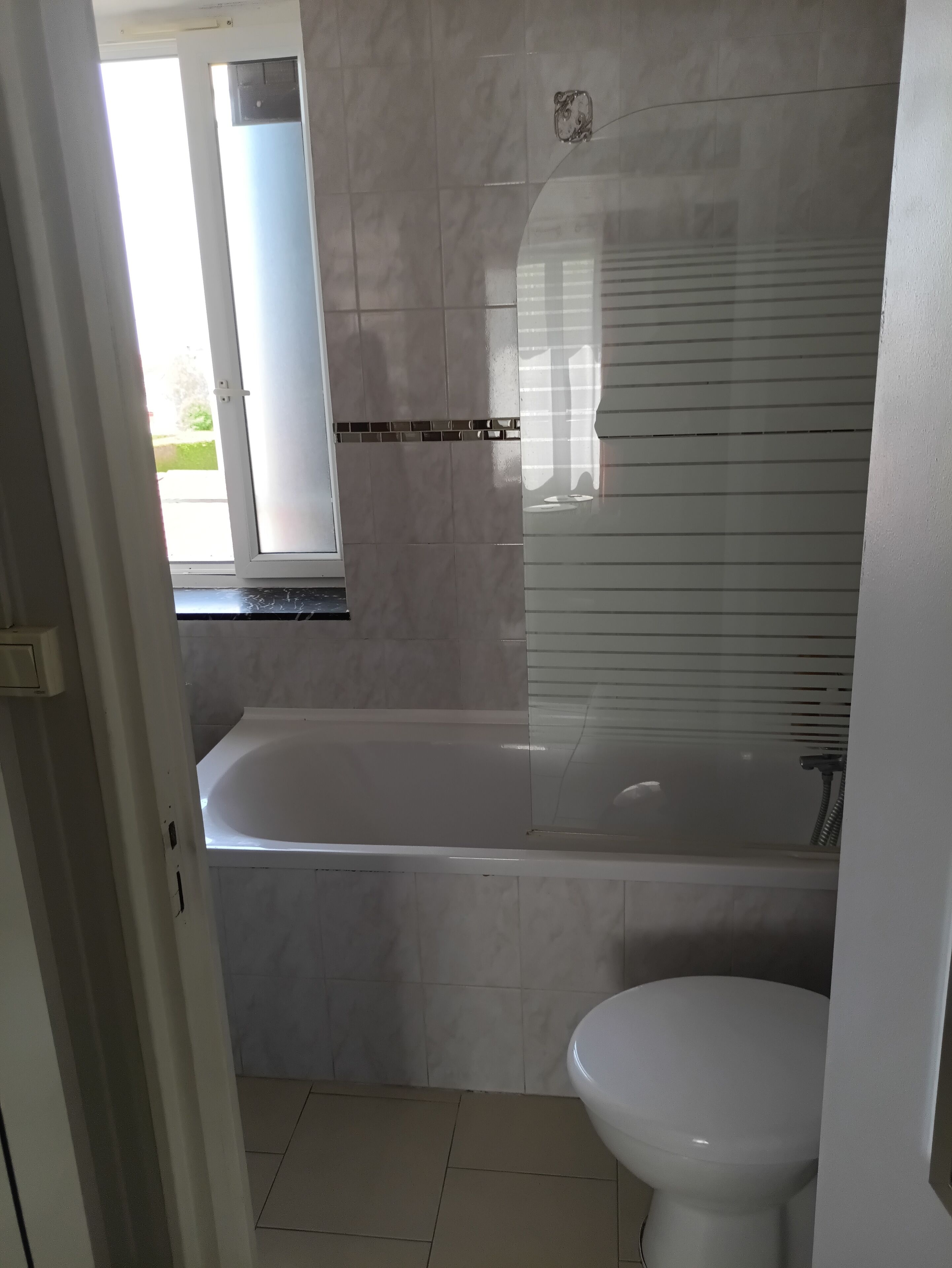 A bathroom with a bathtub, toilet, and a window.