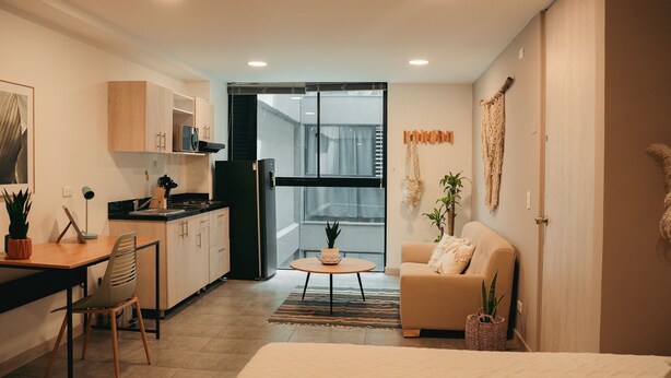 Eine moderne Wohnung mit Küche, Essbereich und Wohnzimmer. Sie verfügt über ein großes Fenster, eine Couch, einen Couchtisch und ein Bett.