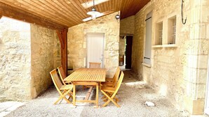 Un bâtiment rustique en pierre, avec une table et des chaises en bois, une porte et une fenêtre avec des volets.