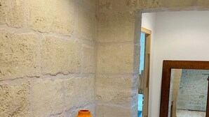 Une pièce avec un banc en bois adossé à un mur en pierre à la texture particulière, un luminaire suspendu et une vue par une fen être dotée d’un cadre en bois.