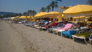 A beach with rows of sunbeds under yellow umbrellas, palm trees, and a clear sky.