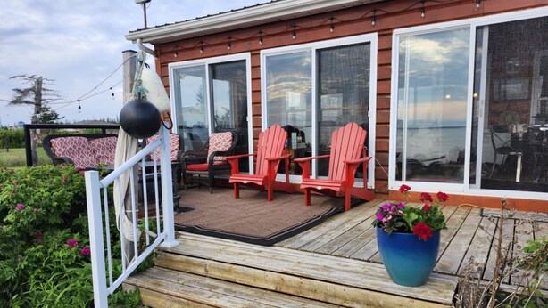 A wooden deck with red Adirondack chairs, a blue flower pot, and a white railing.