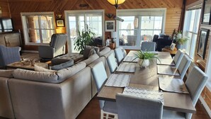 A cozy cabin interior with a wooden ceiling, a sofa, a dining table with chairs, and a television.