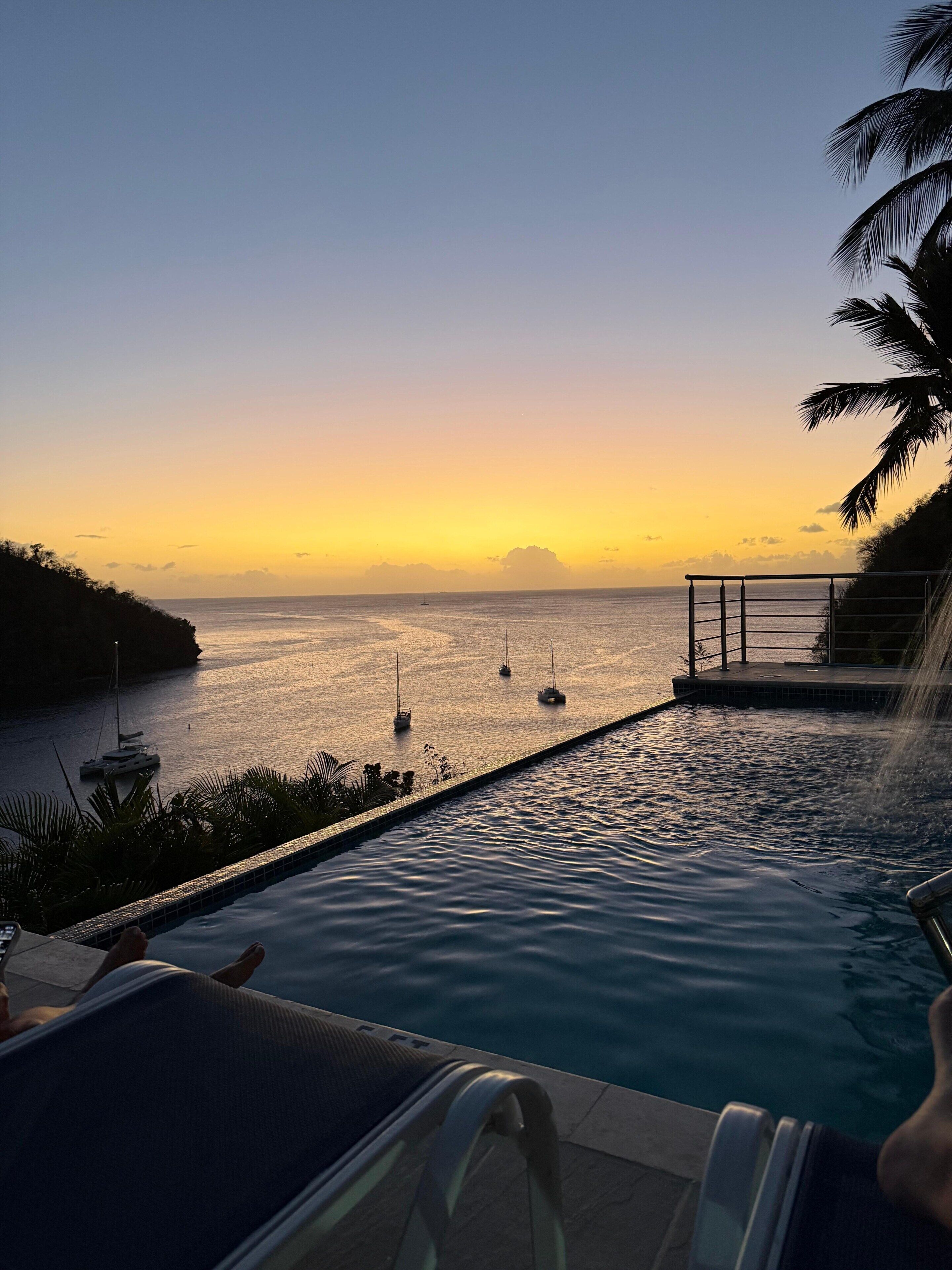 A pool with a view of the sea and boats at sunset.
