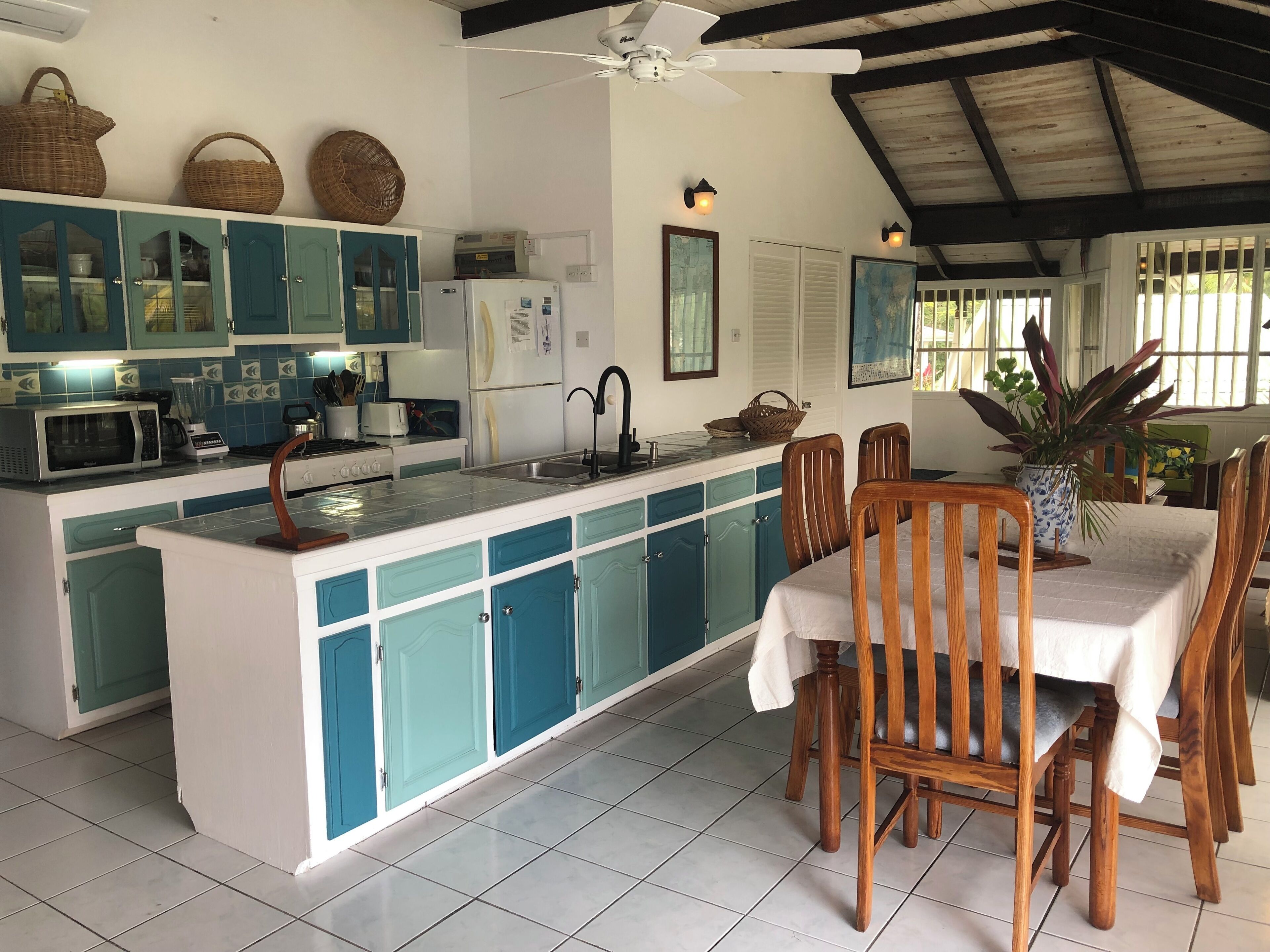 A kitchen with teal cabinets, a white refrigerator, and a dining area with wooden chairs and a table.