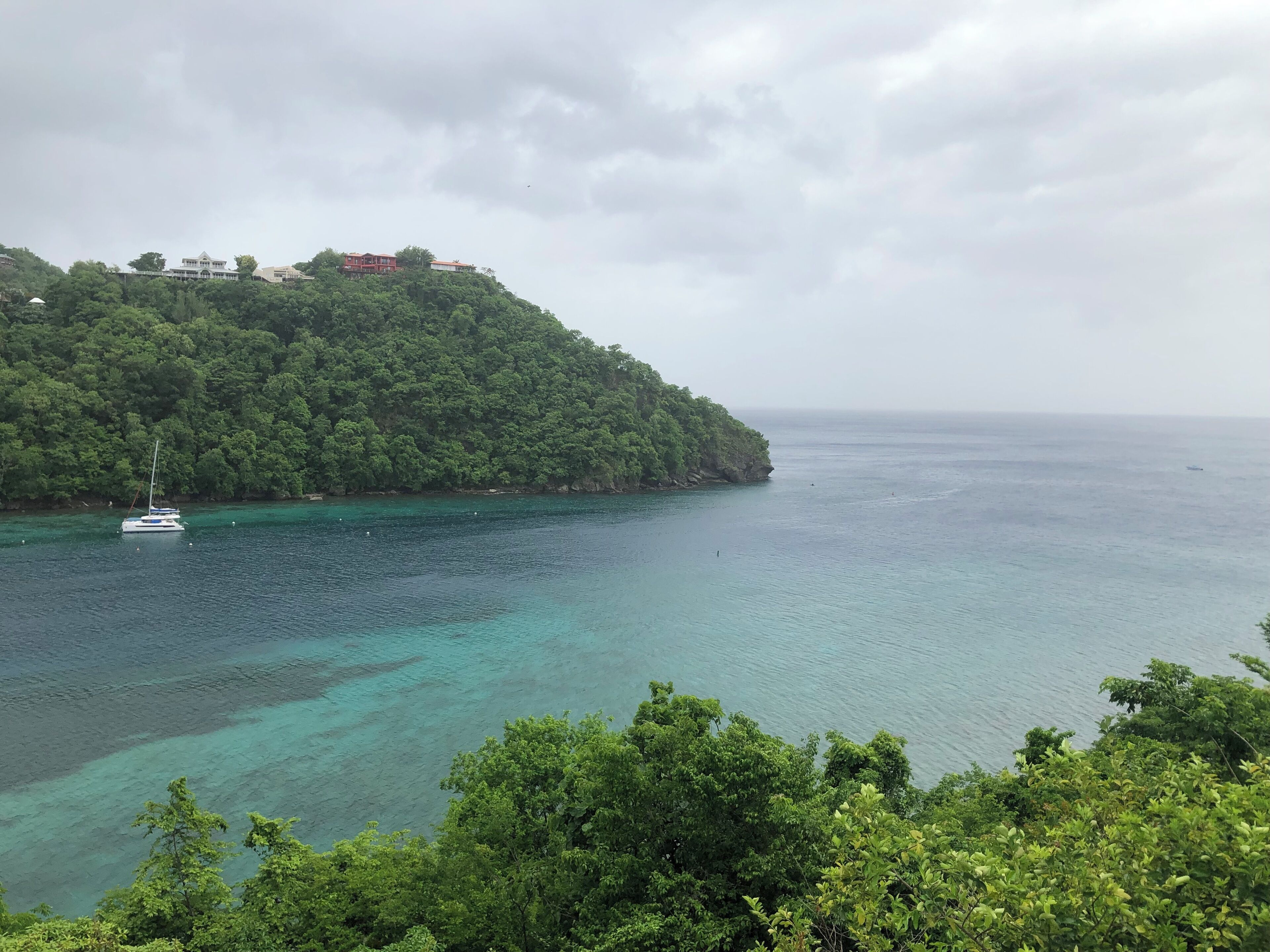 Un paysage côtier avec un bateau ancré près d’une colline verdoyante, dominant une mer calme.