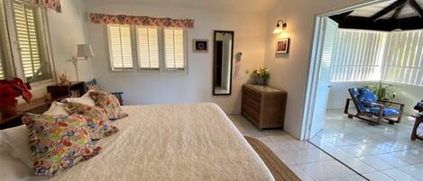 A bedroom with a bed, a ceiling fan, a dresser, a mirror, and a view of the outside.