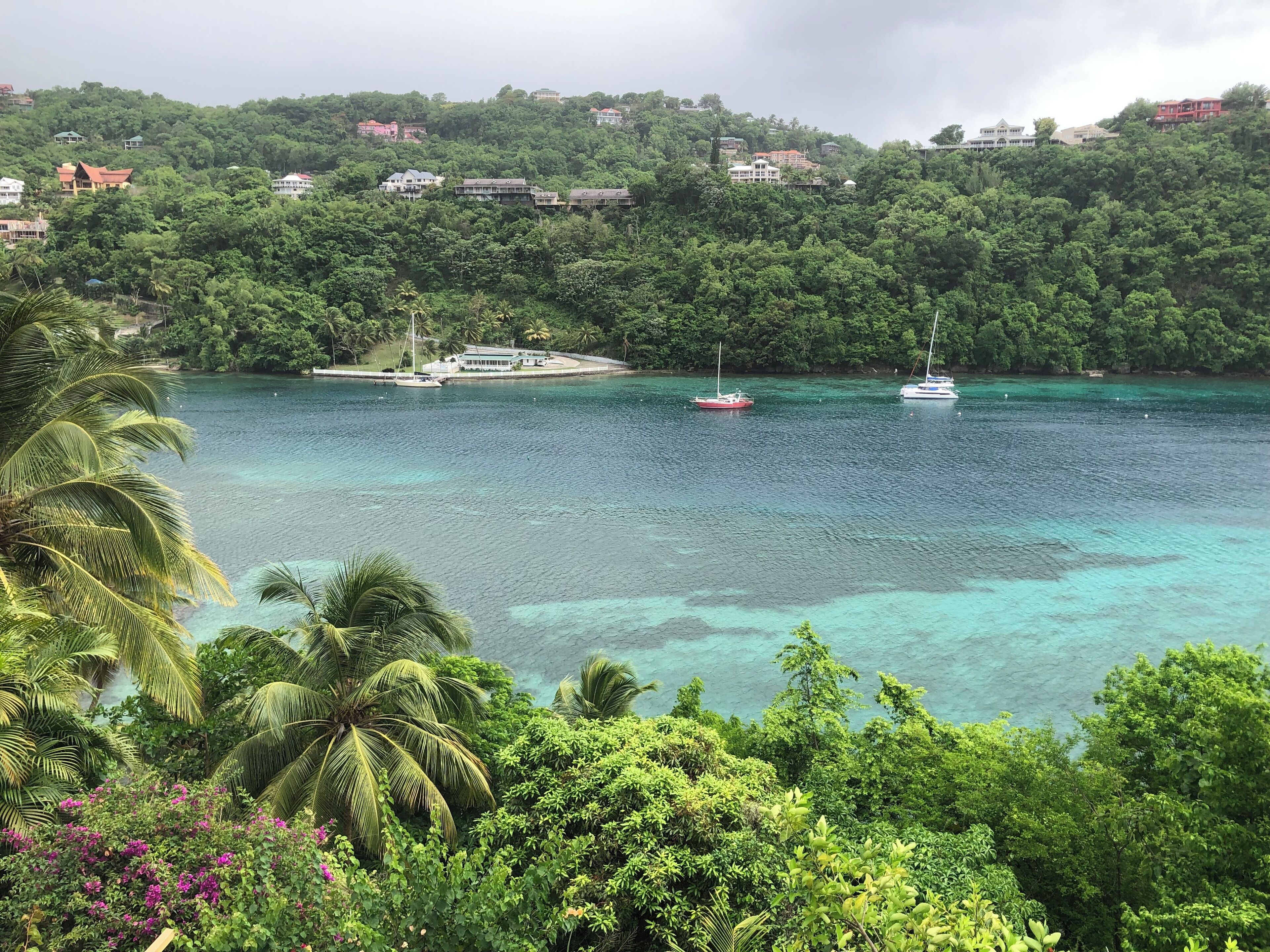 Vista costera con aguas turquesas cristalinas, barcos y vegetación exuberante.