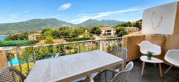 A balcony with a table and chairs, overlooking a mountainous landscape and a pool.