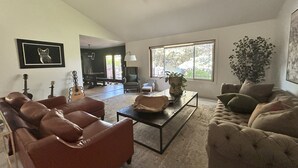 A spacious living room with a large window, a ceiling fan, and a piano. - 4-bedroom house in highly desirable Southside Bozeman with AC and heated garage. (Bozeman)