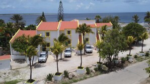 A building with a red roof and white walls, surrounded by palm trees and parked cars.