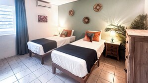 A hotel room with two beds, a nightstand, a lamp, a plant, and a wooden cabinet.