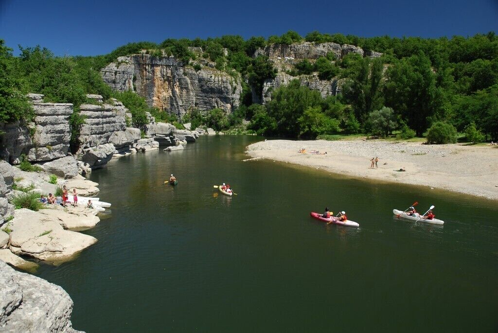 A river with kayaks, rocky cliffs, and a sandy beach.