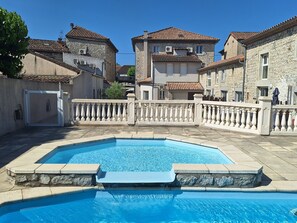 Una piscina con solárium de piedra, rodeada de edificios de piedra con techos de tejas.
