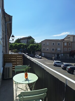 Un balcón con una mesa y sillas, con vista a una calle con coches estacionados y edificios.
