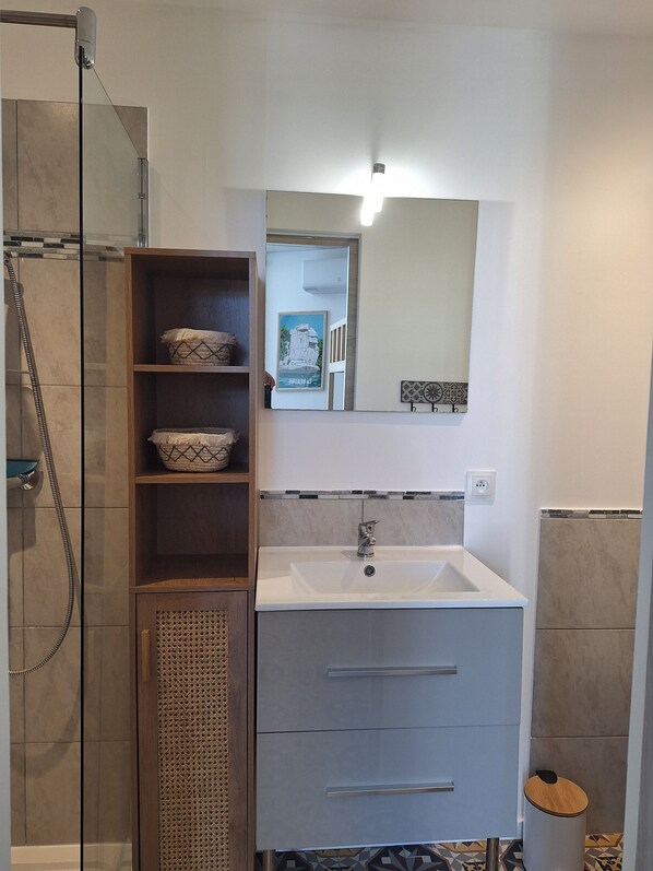 A modern bathroom with a glass shower enclosure, a vanity with a sink and a mirror, and a small trash bin. - Charming studio with a pool in the heart of Ruoms, Ardèche (Ruoms)