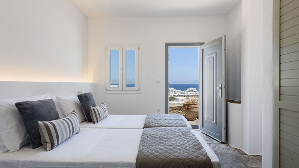 Une chambre avec deux lits, une vue sur la mer et un sol en pierre.