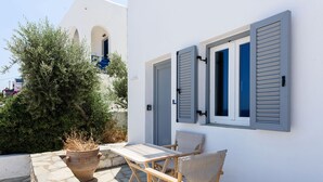 Un bâtiment blanc avec des volets bleus, une table en pierre et deux chaises.
