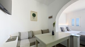Un salon moderne et minimaliste, avec un canapé blanc, une petite table et une vue sur la mer par une fenêtre.