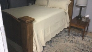 Une chambre à coucher avec un lit en bois, du linge de lit blanc, une table de chevet avec une lampe et un tapis à motifs.