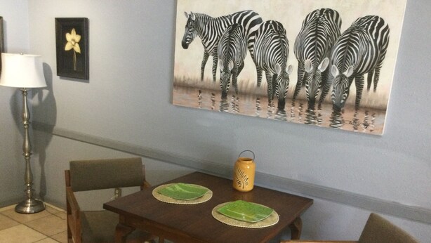 Un coin repas avec une table en bois, quatre chaises, deux sets de table verts, une lanterne jaune et un tableau représentant une zèbre accroché au mur.