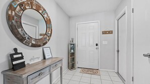 A hallway with a wooden console table, a large mirror, a white door, and a small shelf with decorative items. - Charming 3-bedroom house with WiFi, AC in Palm Harbor (Palm Harbor)