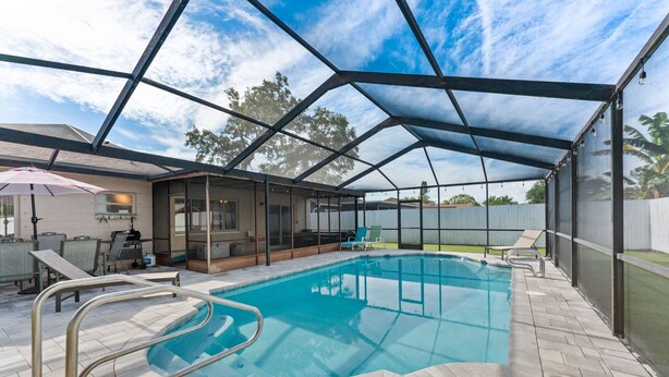 An indoor swimming pool with a covered area, lounge chairs, and a patio with a grill. - Charming 3-bedroom house with WiFi, AC in Palm Harbor (Palm Harbor)