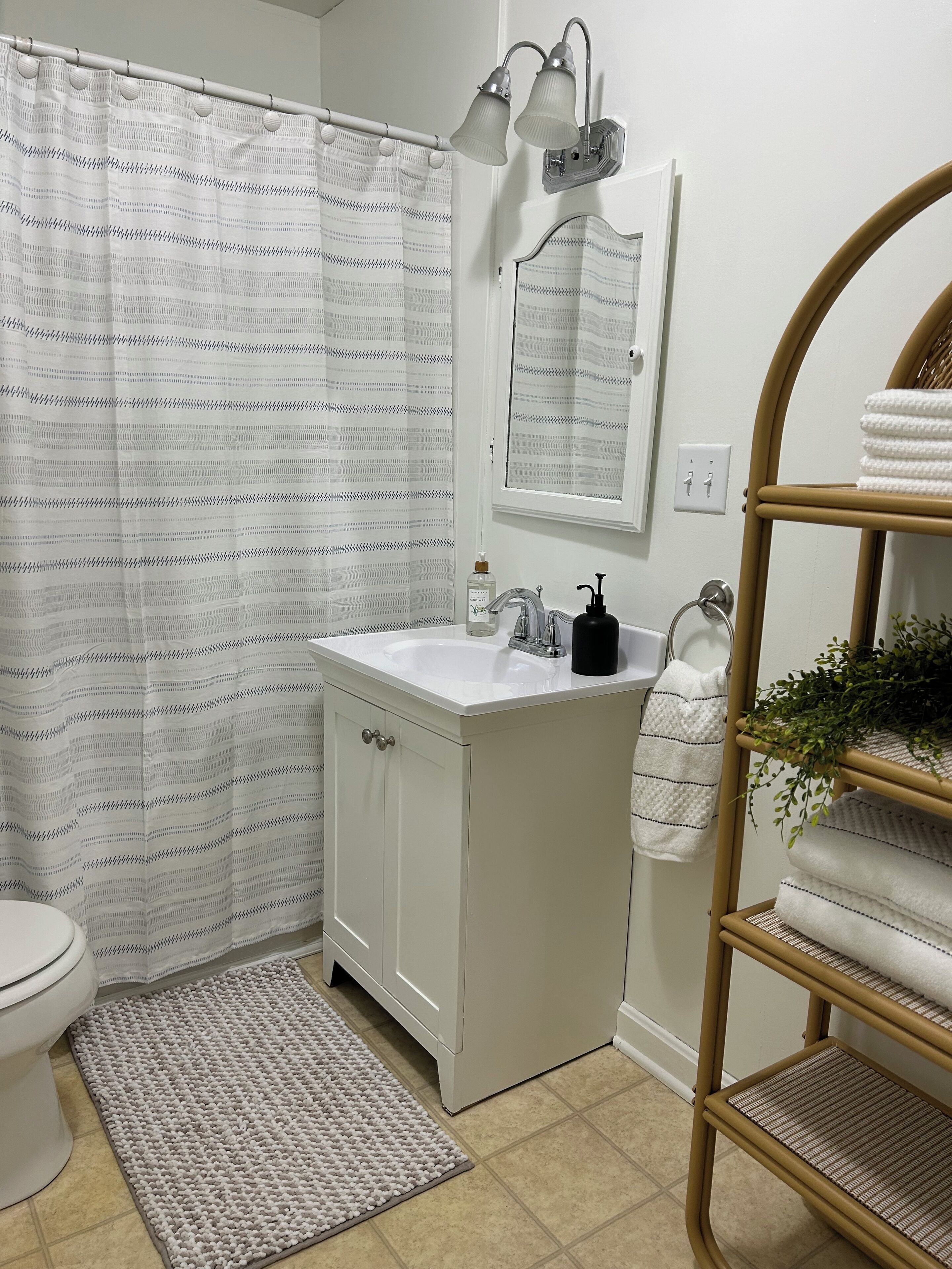 Ein Badezimmer mit Duschvorhang, Waschbecken, Spiegel, Handtuchhalter und einer kleinen Fußmatte.
