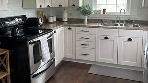 A modern kitchen with white cabinetry, a black stove, and a window with a view. - Cottage in Sugarcreek with Hot Tub (Sugarcreek)