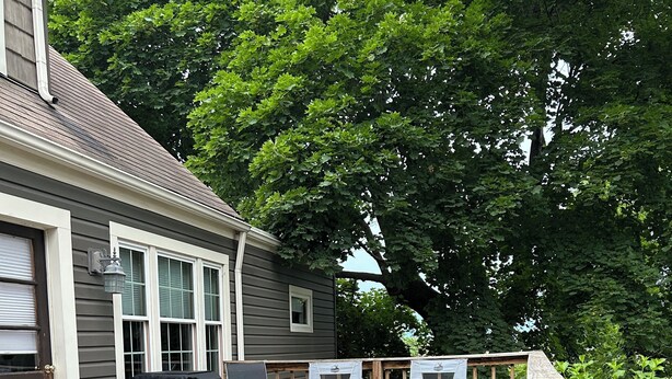 A wooden deck with outdoor furniture, a fire pit, and a garden with red flowers. - Cottage in Sugarcreek with Hot Tub (Sugarcreek)